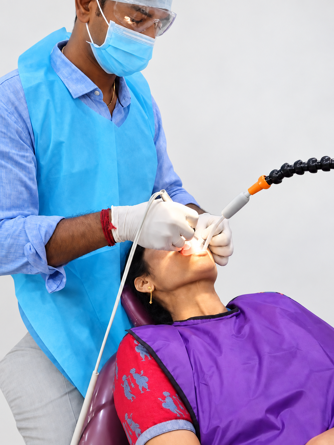 Dentist scaling with both hands while Oraflow Assist holds the suction